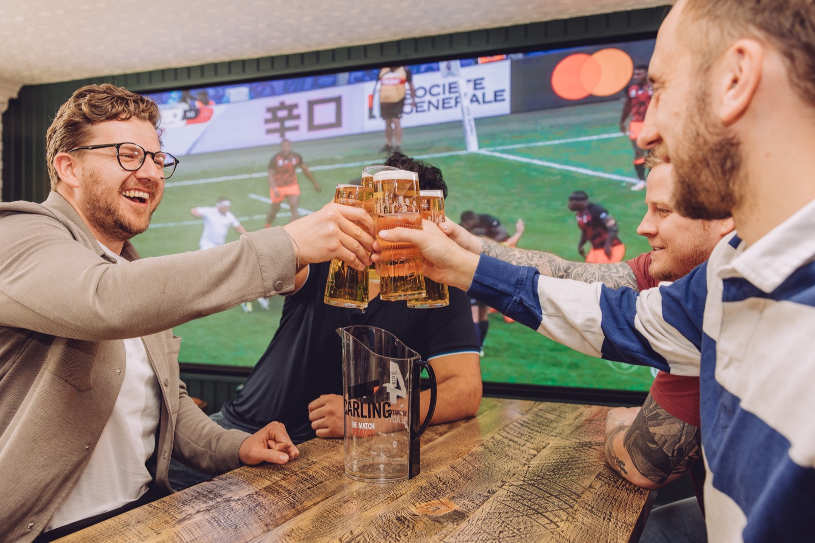 Fans toasting pints in front of a large sports screen